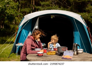 Family, Mother And Child, Having Breakfast In Front Of Pitched Tent In The Forest, While Wild Camping In Norway, Summertime