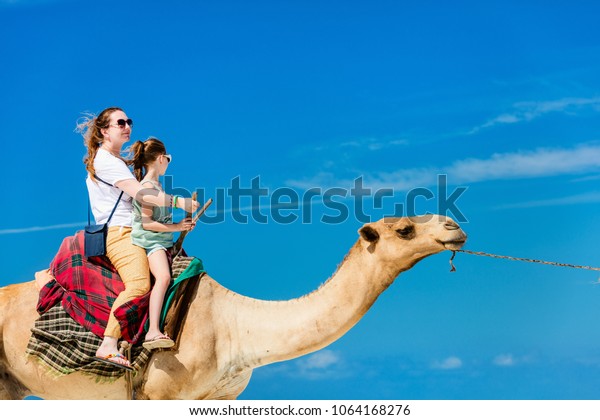 Family mother and daughter riding camel at \
tropical white sand\
beach