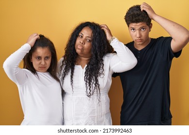 Family Of Mother, Daughter And Son Standing Over Yellow Background Confuse And Wondering About Question. Uncertain With Doubt, Thinking With Hand On Head. Pensive Concept. 