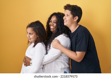 Family Of Mother, Daughter And Son Standing Over Yellow Background Looking To Side, Relax Profile Pose With Natural Face And Confident Smile. 