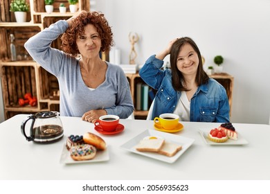 Family Of Mother And Down Syndrome Daughter Sitting At Home Eating Breakfast Confuse And Wonder About Question. Uncertain With Doubt, Thinking With Hand On Head. Pensive Concept. 