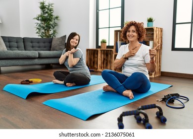 Family Of Mother And Down Syndrome Daughter Doing Exercise At Home Smiling And Looking At The Camera Pointing With Two Hands And Fingers To The Side. 