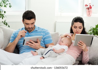 family of mother, father and baby sitting at home with a tablet PC