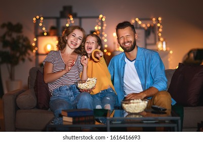 Family Mother Father And Child Daughter Watching Projector, TV, Movies With Popcorn In The Evening   At Home 
