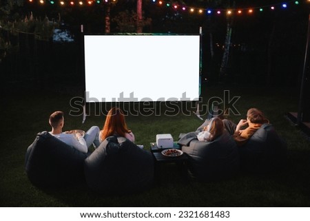 family mother, father and children watch a projector, movies with popcorn in the evening in the courtyard