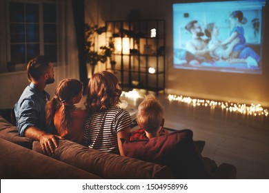 family mother father and children watching projector, TV, movies with popcorn in the evening   at home 
