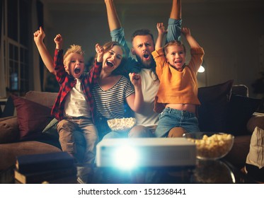 family mother father and children watching projector, TV, movies with popcorn in the evening   at home 