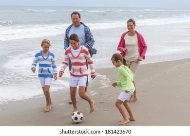 Family Mother, Father, Daughter, Parents And Female Girl Children Having Fun Playing Football Or Soccer On A Beach 