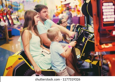 Family Mother, Father And Little Boy Driving Car Arcade In Game Machine At An Amusement Park.