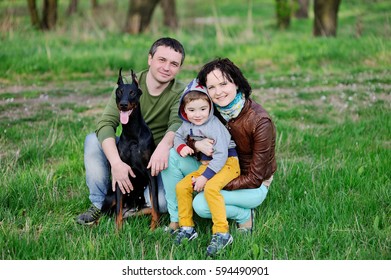 Family - Mother, Father And Little Son With Doberman Dog On The Background Of Spring Forest