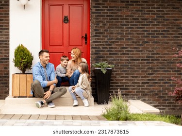 Family with a mother, father, son and daughter sitting outside on steps of a front porch of a brick house - Powered by Shutterstock