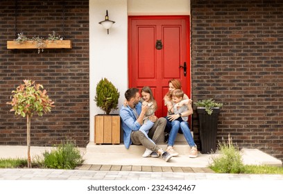 Family with a mother, father, son and daughter sitting outside on steps of a front porch of a brick house - Powered by Shutterstock