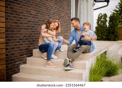 Family with a mother, father, son and daughter sitting outside on steps of a front porch of a brick house - Powered by Shutterstock