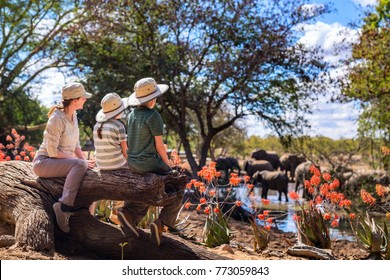 Family Of Mother And Kids On African Safari Vacation Enjoying Wildlife Viewing At Watering Hole