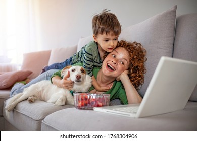 Family - Mother And Son With Laptop On Sofa At Home. Woman And Child Boy Relaxing At Laptop Computer With Dog. Happy Mother And Son Having Fun With A Laptop