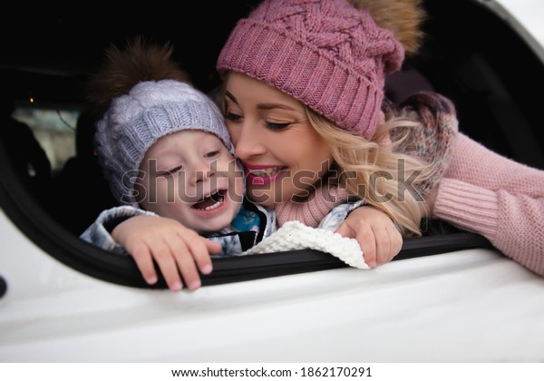 Family, mother and son in warm clothes relaxing in
the car parked in the nature. People dressed sweater and hats  
take a rest in automobile,covered with a blanket in garland
decorated car