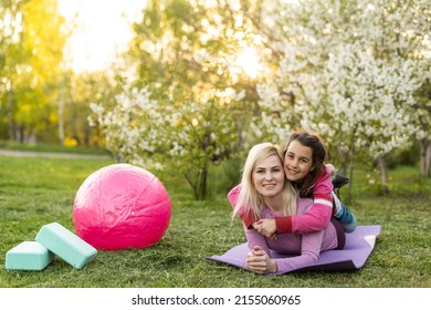 Family Mother Teacher Training Yoga Child Daughter On A Yoga Mat At Home Garden. Family Outdoors. Parent With Child Spends Time Together. Exercise At Home Concept And New Normal.