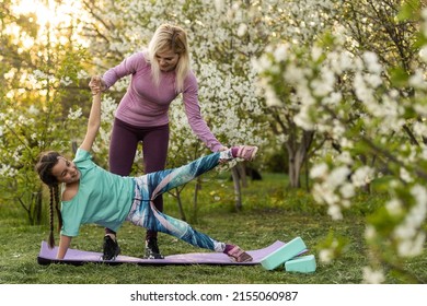 Family Mother Teacher Training Yoga Child Daughter On A Yoga Mat At Home Garden. Family Outdoors. Parent With Child Spends Time Together. Exercise At Home Concept And New Normal.