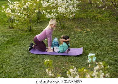 Family Mother Teacher Training Yoga Child Daughter On A Yoga Mat At Home Garden. Family Outdoors. Parent With Child Spends Time Together. Exercise At Home Concept And New Normal.