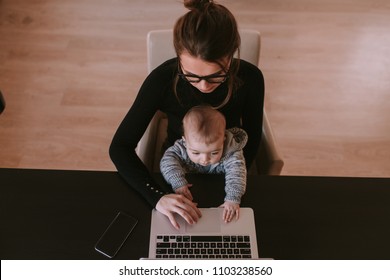 Family, mother working on laptop with child.Top view. Beautiful business mom is using a computer and spending time with her cute baby boy at home. Son and mummy working from home