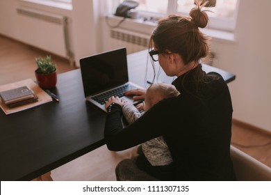 Family, mother working on laptop with child. Top view of woman's and infant hands on notebook. Mom is using a computer and spending time with her cute baby boy at home. Son and mummy working from home