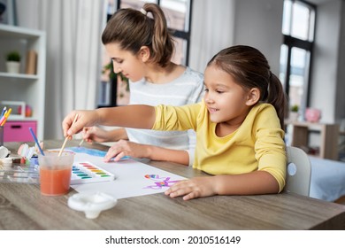 family, motherhood and leisure concept - mother spending time with her little daughter drawing with colors at home - Shutterstock ID 2010516149
