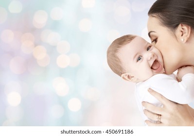 family, motherhood, parenting, people and child care concept - happy mother kissing adorable baby over blue holidays lights background - Powered by Shutterstock