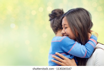 family, motherhood and people concept - happy mother and daughter hugging over green holidays lights background