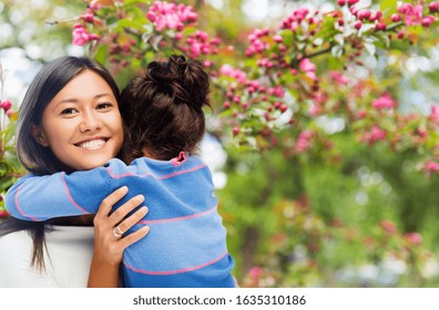 family, motherhood and people concept - happy smiling mother and daughter hugging over cherry blossom background