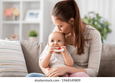 family, motherhood and people concept - happy smiling mother kissing little baby playing with teething toy or rattle at home