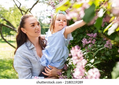 Familienkonzept, Mutterschaft und Menschen - glückliche Mutter mit kleiner Tochter, die im Sommerpark oder Garten lila Blumen berührt