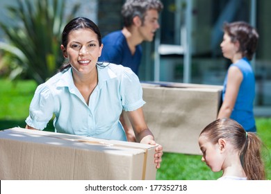 Family Moving Into A New House, Happy Parents With Two Children Carrying Box Smile