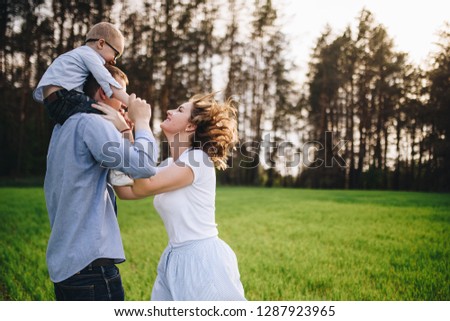 Family in nature. Picnic in the forest, in the meadow. Green grass. Blue clothes. Mom, dad, son with glasses. Boy with blond hair. Joy. Parents play with child. Together. Picnic basket. Food, blanket