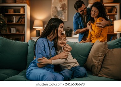 Family observes as a professional home nurse and their child share a warm hug - Powered by Shutterstock