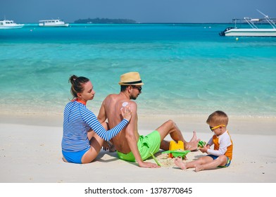 Family On Beach, Young Couple With Three Year Old Boy. Woman Applying Sun Screen Protection Lotion On Man's Back. Summer Vacation At Maldives.