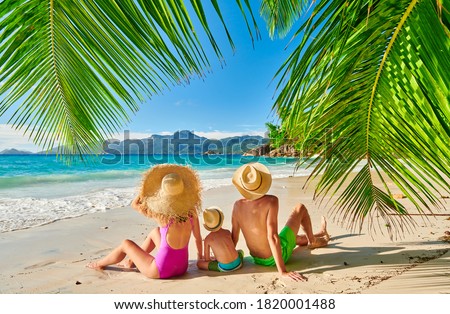 Family on beautiful Anse Soleil beach with palm tree, young couple with three year old toddler boy. Summer vacation at Seychelles, Mahe.