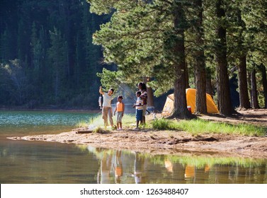 Family On Camping Trip In Forest Catching Fish In Lake