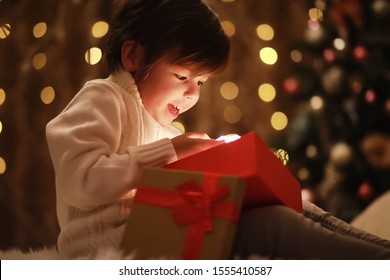 Family On Christmas Eve At Fireplace. Kids Opening Xmas Presents. Children Under Christmas Tree With Gift Boxes. Decorated Living Room With Traditional Fire Place. Cozy Warm Winter Evening Home.