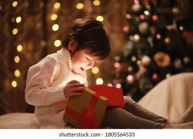 Family On Christmas Eve At Fireplace. Kids Opening Xmas Presents. Children Under Christmas Tree With Gift Boxes. Decorated Living Room With Traditional Fire Place. Cozy Warm Winter Evening Home.