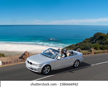 Family on holiday driving convertible on road with beach and ocean in background - Powered by Shutterstock