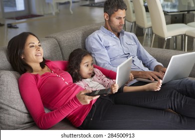 Family On Sofa With Laptop And Digital Tablet Watching TV