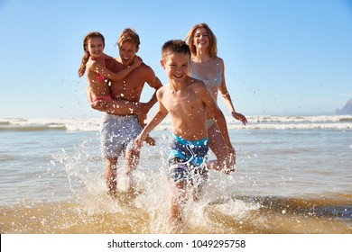 Family On Summer Beach Vacation Run Out Of Sea Towards Camera