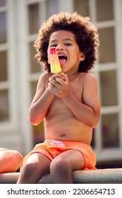 Family On Summer Holiday With Boy Eating Ice Lolly Splashing At Edge Of Swimming Pool