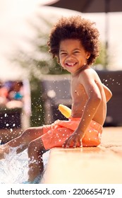 Family On Summer Holiday With Boy Eating Ice Lolly Splashing At Edge Of Swimming Pool