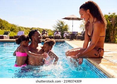 Family On Summer Holiday With Two Girls Being Held In Swimming Pool By Dad Splashing Mum - Powered by Shutterstock