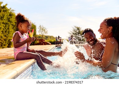 Family On Summer Holiday With Two Girls Eating Ice Lollies By Swimming Pool Splashing Parents