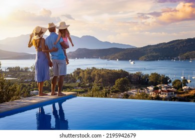 A family on summer holidays stands by the swimming pool and enjoys the beautiful sunset behind the mountains and the sea - Powered by Shutterstock