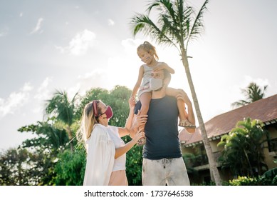 Family On A Walk In The Park In Protective Masks Against The Corona Of The Virus Covid-19. Sunny Day On The Background Of Palm Trees.
