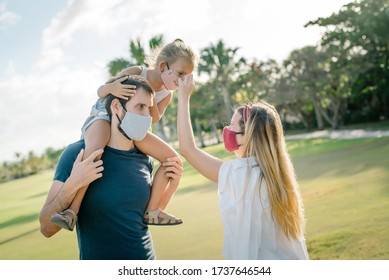 Family On A Walk In The Park In Protective Masks Against The Corona Of The Virus Covid-19. Sunny Day On The Background Of Palm Trees.
