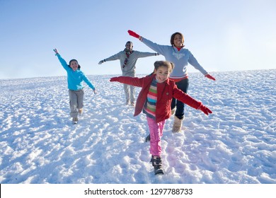 Family on winter vacation running down snowy hill smiling at camera